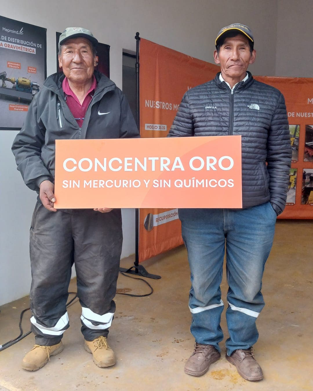 Dos mineros en el taller Meproind sosteniendo el cartel «Concentra oro sin mercurio y sin químicos»